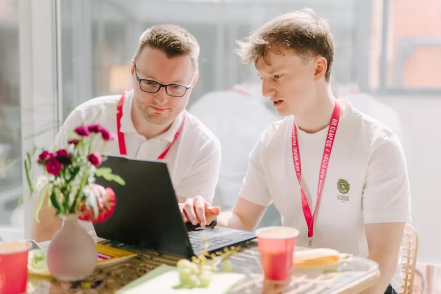 Ein erfahrener und ein junger Teilnehmer schauen beim HR CAMPUS gemeinsam auf einen Laptop